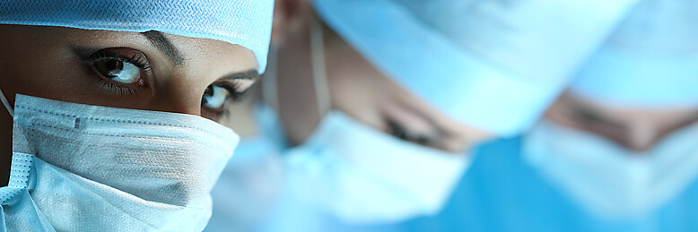 Portrait einer Frau mit Kopf- und Mundschutz aus einem Operationssaal im Anschnitt