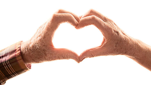 Alte Männerhand und alte Frauenhand, die gemeinsam ein Herz formen.
